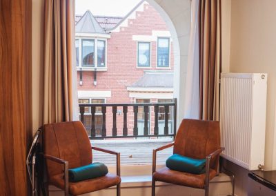 Tweepersoonskamer met zicht op balkon met gordijnen en deuren open - Hotel Eckhardt Uithuizen